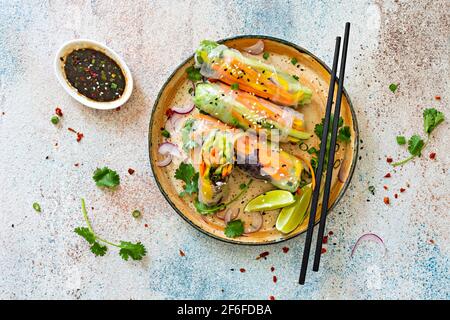 Frische asiatische Vorspeise Frühlingsrollen (Nem) aus Reispapier und rohem Gemüse und Kräutern mit heißer Sauce auf hellblauem Hintergrund. Vietnamesische Küche Stockfoto