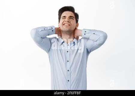 Büroangestellter, Mitarbeiter, die Rückenschmerzen haben, Halsschmerzen berühren und durch schmerzhaftes Gefühl nach dem Sitzen auf der Arbeit grimacing, haben Beschwerden und stehen darüber Stockfoto