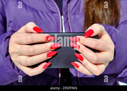 Das Mädchen dreht heimlich mit einer Smartphone-Kamera und versteckt die Linse zwischen ihren Fingern für Geheimhaltung; Konzept der Geheimhaltung, Tarnung und Verfolgung Stockfoto