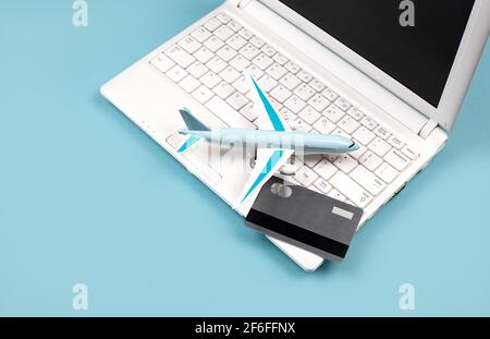 Weißes Notebook auf blauem Hintergrund. In der Nähe befindet sich eine Bankkarte und ein Miniaturflugzeug. Konzept - Online-Buchung von Flugtickets, Reiseplanung. Stockfoto