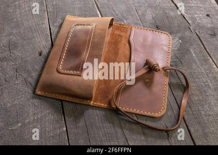 Handgemachte braune Tabaktasche aus Leder auf Holzhintergrund. DIY. Stockfoto