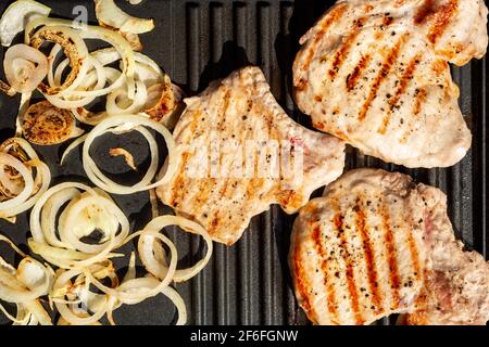Draufsicht auf Schweinekoteletts und zischende Zwiebeln auf dem tragbaren Gerät Elektrischer Mini Grill Hausmannskost im Freien Stockfoto