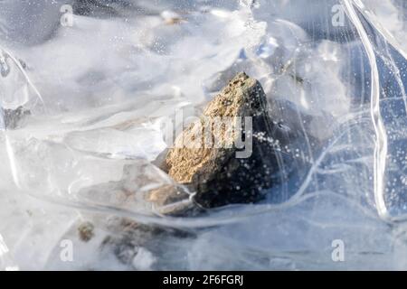 Unter dem durchsichtigen Eis wird ein Stück Fels eingefroren. Nahaufnahme Hintergrundstruktur Stockfoto