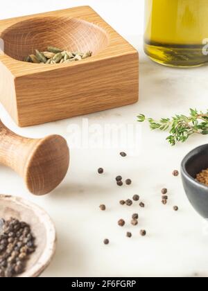 Kräuter und Gewürze kochen auf einem Marmortisch. Holzmörtel und Burgpfropfen sowie verschiedene Gewürze und Kräuter. Vorderansicht. Speicherplatz kopieren Stockfoto