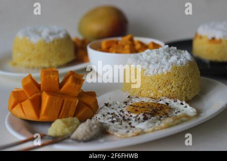 Gedämpfter gemahlener Reis, geschichtet mit Kokosraspeln und Mango. Lokal bekannt als Mango Puttu. Serviert mit gebratenem Ei, der sonnigen Seite nach oben, mit Zucker und g Stockfoto