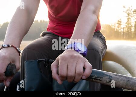 Frauen halten die Ruder fest und rudern in einem aufblasbaren Boot entlang des Sees vor dem Hintergrund von Nebel, Sonnenaufgang und Wald. Stockfoto