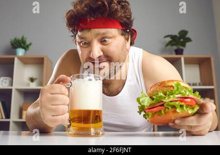 Aufgeregter, verrückter, fetter Mann, der Bier trinkt und Burger isst Hochformat Stockfoto