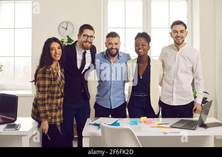 Ein positives Lächeln auf den Lippen, ein vielfältiges Geschäftsteam, das sich umarmt und die Kamera anschaut Büro Stockfoto
