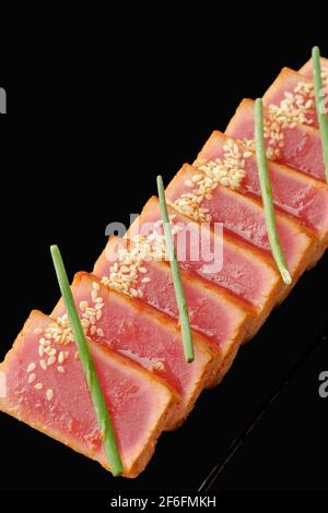 Mittelgroßer Thunfisch-Tataki, Kimchi-Sauce, Aroy-D-Sauce, Schnittlauch, Sesam. Isoliert auf schwarzem Hintergrund Stockfoto