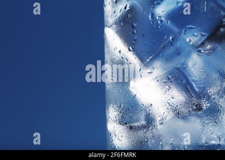 Eiswürfel in einem vernebelten Glas mit Tropfen Eiswasser Nahaufnahme Makro. Erfrischendes und kühlendes Getränk bei heißem Wetter. Blauer Hintergrund. Vollbild Stockfoto