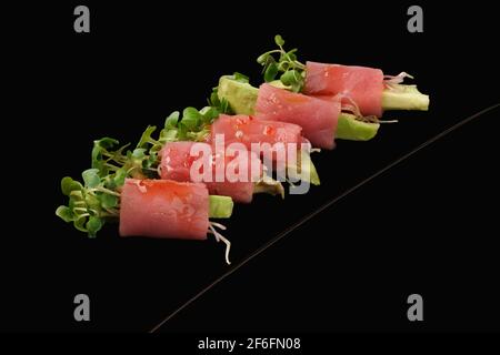 Rollen Sie mit frischem Thunfisch, Avocado, Microgreen. Isoliert auf schwarzem Hintergrund. Stockfoto