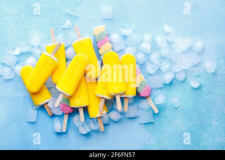 Exotische Fruchteis-Sticks auf blauem Hintergrund mit Eiswürfeln. Draufsicht, Leerraum Stockfoto