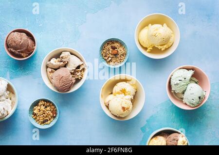 Verschiedene Eisdesserts in Schüsseln auf rustikalem blauen Hintergrund, Draufsicht, Leerraum Stockfoto