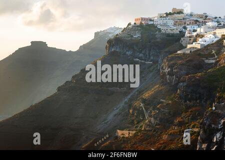 Sonnenuntergang auf der griechischen Insel Santorini, mit farbenfrohem warmen Licht und Wolken über der Stadt. Der Blick folgt dem Rand der Caldera von Thira Stockfoto