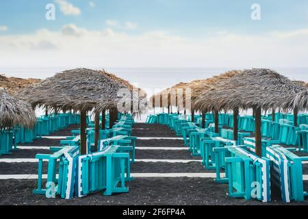 Perissa Black Sand Beach, Santorini, Griechenland am Morgen. Am Strand Strohschirm und Strandliegen mit Meerblick Stockfoto