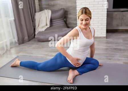 Junge schwangere Dame macht Fitness und Yoga Übungen auf grauen Matte zu Hause. Gesunde Schwangerschaft, Sport und Lifestyle-Konzept. Frau erwartet Baby, Blei Stockfoto