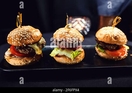 Drei Mini-Burger auf einem schwarzen rechteckigen, länglichen Ständer. Stockfoto