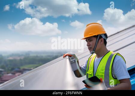 Nahaufnahme asiatischer Techniker, der die Wartung der Sonnenkollektoren auf dem Dach überprüft, Solarenergie Stockfoto