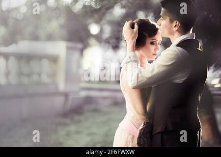 Ein Paar im Retro-Kleid steht vor einem großen Baum und einem Zaun. Ein Mann passt die Haare auf dem Kopf einer Frau an. Historische Rekonstruktion der 1930er Jahre. Stockfoto