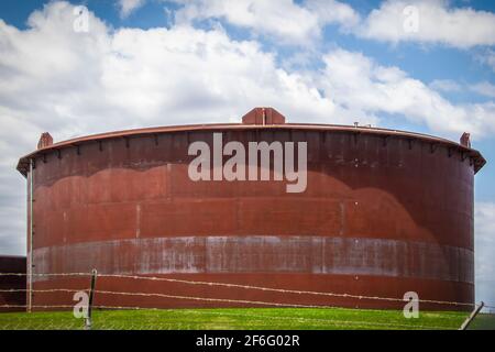 Riesiger rostiger Öltank in Tanklager in Cushing, Oklahoma Hinter Stacheldrahtzaun mit hübschem blauen Himmel Hintergrund Stockfoto