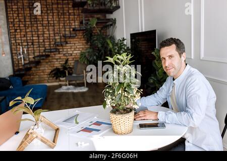 Ein stilvoller, freiberuflicher Mitarbeiter mit einem Laptop arbeitet im Heimbüro an Projekten oder Finanzberichten. Ein gutaussehender, selbstbewusster Geschäftsmann ist Stockfoto