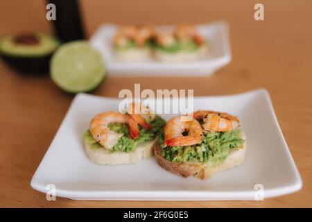 Gesunde Vorspeise von Bruschetta mit Guacamole Garnelen Nahaufnahme zu sehen. Gebratene Shrimps und pürierte Avocado auf einem gerösteten Brot Stockfoto