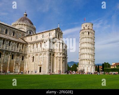 Schiefer Turm von Pisa (aufwendig geschmückter Turm aus dem 14. Jahrhundert) und Kathedrale von Pisa (marmorgestreifte Kathedrale) auf sommerlich grünem Gras und blauem Himmel. Tr Stockfoto