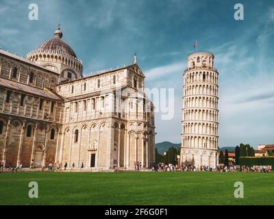 Schiefer Turm von Pisa (aufwendig geschmückter Turm aus dem 14. Jahrhundert) und Cattedrale di Pisa (marmorgestreifte Kathedrale) auf sommerlich grünem Gras und blauem Himmel. T Stockfoto