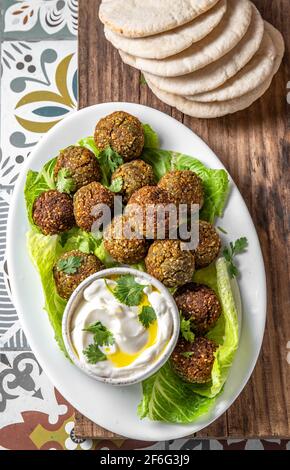 Traditionelle hausgemachte Kichererbsenfalafel Kugeln mit weißer Sauce und Pita Brot auf Weißblech auf Holzbrett, gesunde vegetarische Lebenskonzept. Israel Stockfoto