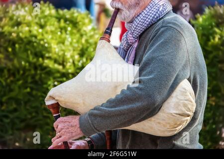 Älterer bärtiger Mann ist Pullover und Schal, der altes Schaffell spielt Dudelsack im Freien - abgeschnitten und selektiver Fokus Stockfoto