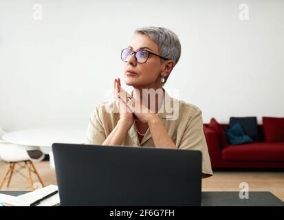 Stilvolle reife Frau in Brille am Schreibtisch sitzen Stockfoto