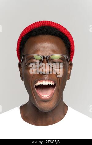 Lachend positiver junger afrikanischer Hipster-Mann in Brille und Rot hut gut gelaunt mit geschlossenen Augen Stockfoto