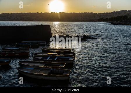 Alte hölzerne Fischerboote, die bei Sonnenuntergang auf dem Golf von Neapel, Italien, auf einem Pier neben dem Castel dell'Ovo (Egg Castle) festgemacht wurden Stockfoto