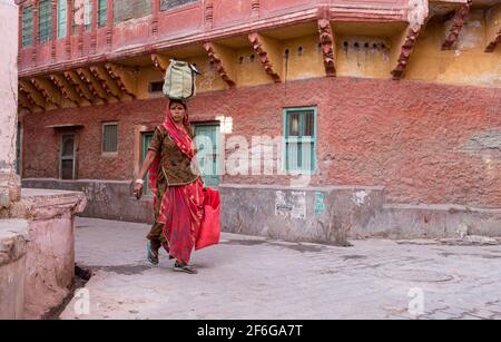 Frau trägt Lebensmittel auf dem Kopf in den Straßen der blauen Stadt Jodhpur in Rajasthan, Indien Stockfoto