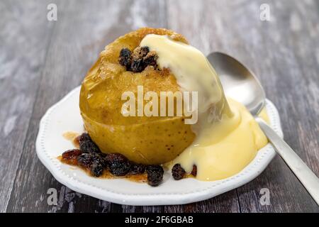 Gebackener Apfel mit Sultaninen und braunem Zucker mit Pudding garniert Stockfoto