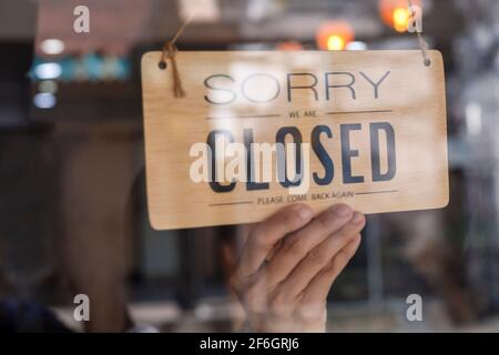 Hand des asiatischen Besitzers Einzelhandel, Café Frau drehen Schild zu geschlossen. Schutz vor einer Pandemie des Coronavirus. Schließen Sie den Laden, das Restaurant oder den Pub Stockfoto