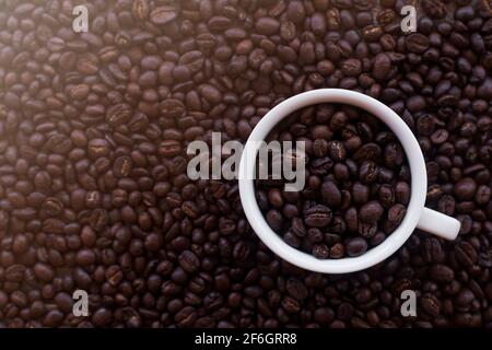 Kaffeetasse mit gerösteten Bohnen auf dem Hintergrund der Kaffeebohnen. Draufsicht mit Kopierbereich. Draufsicht Kaffeebohnen Hintergrund mit weißer Kaffeetasse Stockfoto