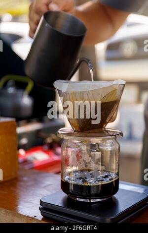 Barista verschüttet heißes Wasser Bereiten Sie Filterkaffee von der Edelstahl-Teekane bis zur Tropfpapiermaschine auf schwarzen einfachen Gewichten zu. Alles dick Holztisch Stockfoto