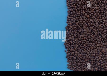 Draufsicht braun geröstete Kaffeebohnen auf blauem Hintergrund verstreut. Kaffeebohnen auf halbblauem Hintergrund mit Kopierplatz Stockfoto