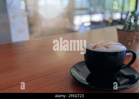 Nahaufnahme von heißem Cappuccino, Latte, Caramel Macchiato auf dem Tisch mit Blur Coffee Shop Hintergrund. Verfahren Sie mit warmen vintage Ton Stil. Stockfoto