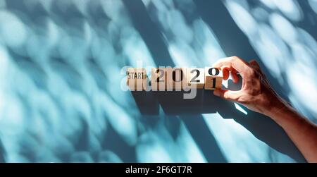 Hand hält Holzwürfel mit Flip-over-Block beginnen 2020 bis 2021 Wort auf blau und Schatten Hintergrund. Draufsicht Hand Flip Holzblock mit Nummer Text st Stockfoto