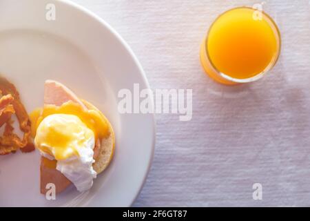 Draufsicht close up Orangensaft im Glas und Ei benedict Frühstück auf weißem Tischdecke. Essen und Trinken Konzept.Draufsicht Frühstück mit pochierten Eiern ro Stockfoto