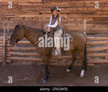 Eine junge attraktive, arbeitende Cowgirl-Wranglerin posiert auf ihrem Pferd auf einer Ranch in der Nähe von Moab, Utah. Sie trägt Lederbeine, um sie vor dornigen Bürsten zu schützen Stockfoto