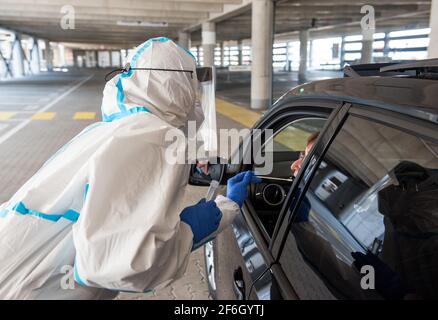 Hamburg, Deutschland. März 2021. Ein Mitarbeiter nimmt während eines Probelaufes für ein Durchfahrzentrum am Flughafen einen Tupfer aus dem Hals einer weiblichen Fahrerin für einen Corona-Test mit. Eine Parkgarage am Flughafen bietet nun die Möglichkeit, sich auf das Corona-Virus in Ihrem Auto testen zu lassen. Quelle: Daniel Bockwoldt/dpa/Alamy Live News Stockfoto