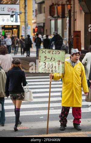 Männliche menschliche Plakatwand mit gelbem Regenmantel, die vor der Zebrakreuzung, Akihabara, Tokio, Japan, steht Stockfoto