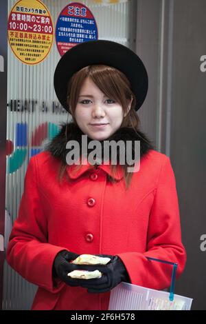 Hübsches Promo-Mädchen in gelesenen Mantel mit Pelzkragen, das Werbematerial verteilt, Ginza, Tokio, Japan Stockfoto