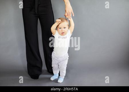 Lächelnd schöne Frau mit ihrem elfmonatigen Baby auf grauem Hintergrund. Mutterschaftskonzept Stockfoto