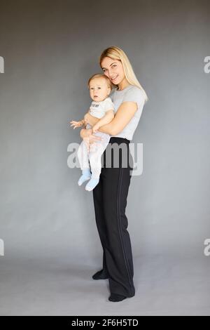 Lächelnd schöne Frau mit ihrem elfmonatigen Baby auf grauem Hintergrund. Mutterschaftskonzept Stockfoto