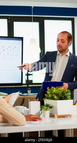 Manager zeigt auf digitales, interaktives Whiteboard mit Wachstumsanalyse, Diagrammen, Statistiken und Daten. Verschiedene Personen, die während einer Konferenz im Broadroom arbeiten und über Unternehmensprobleme sprechen. Stockfoto