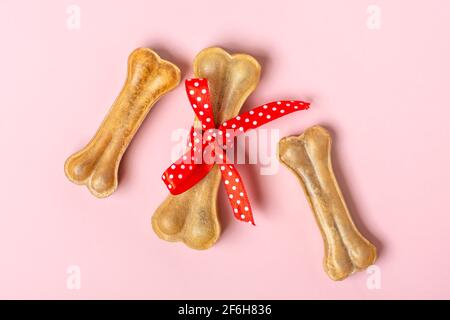 Knochen für Hunde mit roter Schleife isoliert auf rosa Hintergrund Draufsicht Flat Lay Delicious Leckerbissen für Ihr geliebtes Haustier Food for Animals Konzept. Stockfoto